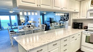 A modern kitchen with white cabinetry, a large island, and a view to a balcony. - Ocean Front Amelia Island, Beachfront Pool, 20% Off Sunglasses at Eye Envy store (Fernandina Beach)
