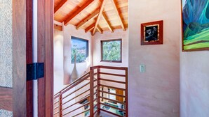 Un escalier en bois avec une rampe en métal, une vue sur l’extérieur par les fenêtres et un tableau accroché au mur.
