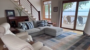 A living room with a sofa, two recliners, a coffee table, a patterned rug, a staircase, and a view of a deck with chairs. - Lakefront Retreat near Saratoga Racetrack, SPAC (Malta)