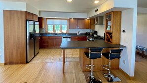 A modern kitchen with wooden cabinets, stainless steel appliances, and a central island with bar stools. - Lakefront Retreat near Saratoga Racetrack, SPAC (Malta)