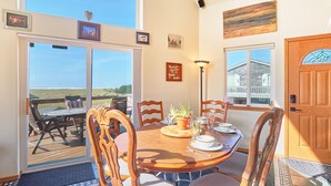 Un coin repas avec une table et des chaises en bois, une vue sur l’océan et un panneau « Interdiction de fumer » sur la porte.