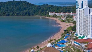 Un complejo turístico costero con playa, varias piscinas y un gran edificio de hotel.