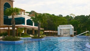 Una piscina con fuente, rodeada de palmeras y un edificio con ventanales amplios.