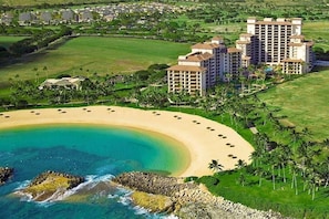 Vista aérea de um resort com praia, vários edifícios altos e uma área gramada bem cuidada.