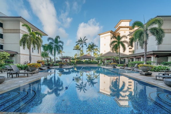 Piscina com espreguiçadeiras e palmeiras, cercada por edifícios.