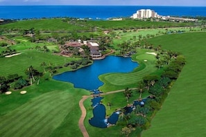 Um campo de golfe com um lago grande, um clube e um hotel ao fundo.