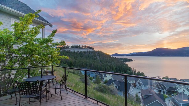 Une terrasse avec une table et des chaises, donnant sur un lac et des collines boisées.