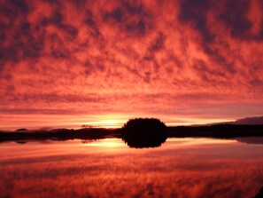 Un atardecer sobre un lago tranquilo con el silueta de una isla boscosa en el centro.