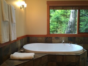 Un baño con bañera, ventana con vistas al bosque y toallas colgadas en la pared.