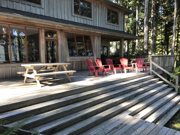 Una terraza de madera con una mesa de picnic y sillas Adirondack rojas.