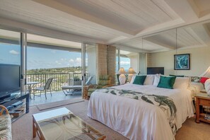 A bedroom with a large bed, a balcony with outdoor seating, and a television. - *~* Sky High *~* Ocean View Studio (Lahaina)