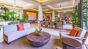 Een ruime lobby met een bank, een rond bijzettafeltje en stoelen, met grote ramen en kamerplanten.