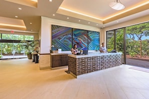 Un espace d’accueil au design moderne, comprenant un comptoir de réception, une grande peinture abstraite et de grandes fenêtres donnant sur un paysage verdoyant.