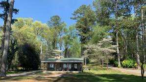 Une cabane dotée d’un toit végétalisé, entourée d’arbres et d’une zone herbeuse.
