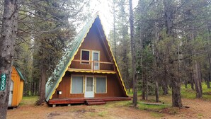 A cabin with a triangular roof, a front porch, and a small adjacent shed.