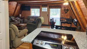 A cozy cabin interior with a kitchen area featuring a stove, dining table, and chairs.
