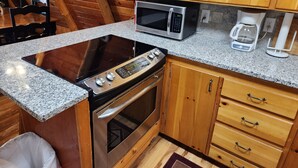A compact kitchen with a built-in microwave, stove, and oven. There is a coffee maker and a trash bin.