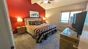 A bedroom with a bed, nightstands, a lamp, a dresser, a ceiling fan, and a window.
