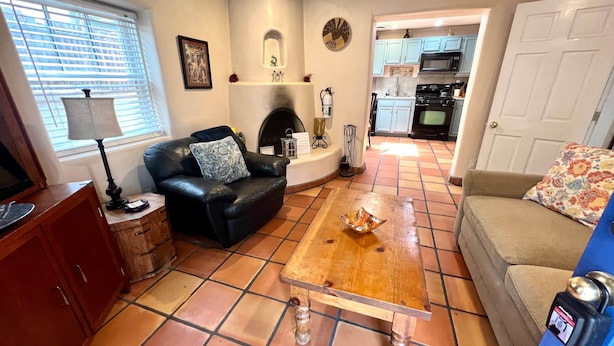 Ein Wohnzimmer mit Kamin, Couch und Couchtisch. Im Hintergrund ist eine Küche zu sehen.