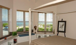 A bedroom with a large bed, a window with a view of the beach, a desk with a lamp, and a framed picture on the wall. - Oceanfront, Pool, Gourmet Kitchen, 2 BR, Office with Futon. (Bamboo Bay)