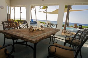 A covered outdoor dining area with a mosaic table, chairs, and a view of the ocean. - Oceanfront, Pool, Gourmet Kitchen, 2 BR, Office with Futon. (Bamboo Bay)