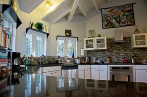 A modern kitchen with a large island, white cabinets, a stone backsplash, and a painting above the stove. - Oceanfront, Pool, Gourmet Kitchen, 2 BR, Office with Futon. (Bamboo Bay)