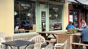 An outdoor seating area with plastic chairs and tables in front of a tea bar with a red awning.