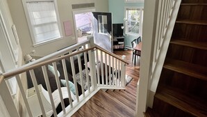A staircase with wooden steps and white railings leading to a room with a ceiling fan, a television, and a dining area with a table and chairs.