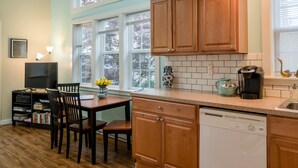 A kitchen with wooden cabinets, a dishwasher, a coffee maker, and a dining area with chairs and a table.