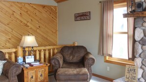 A cozy room with a leather armchair, a wooden cabinet with a Wi-Fi sign, and a stone fireplace. - Views of Grand Lake, Shadow Mountain Lake and RMNP! (Grand Lake)