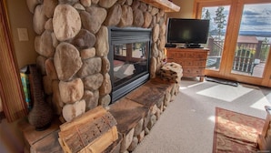 A stone fireplace with a TV, wooden shelves, and a view of the outdoors. - Views of Grand Lake, Shadow Mountain Lake and RMNP! (Grand Lake)
