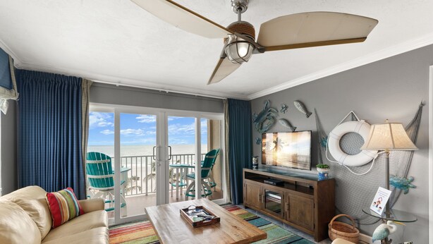 Een ruime woonkamer met een grote bank, een salontafel en een televisie. Er is een balkon met uitzicht op de oceaan.