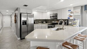 Een moderne keuken met witte kasten, roestvrijstalen apparatuur en een groot kookeiland met barkrukken.
