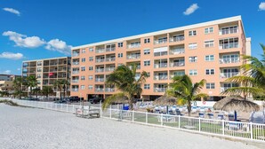 Een meerhoog hotel met balkons, een zandstrand ervoor en palmbomen.