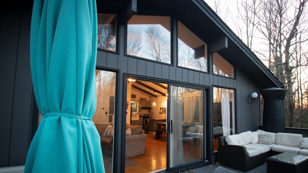 Ett modernt hus med en stor glasdörr som leder in till ett vardagsrum med en soffa och ett matbord.