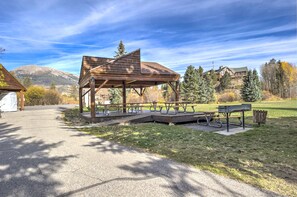 A wooden pavilion with picnic tables in a park with mountains in the background.