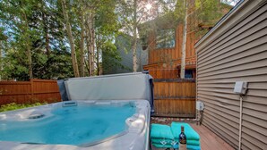 Un bain à remous avec une terrasse en bois, une table avec une bouteille et des verres, et une clôture en bois en arrière-plan.