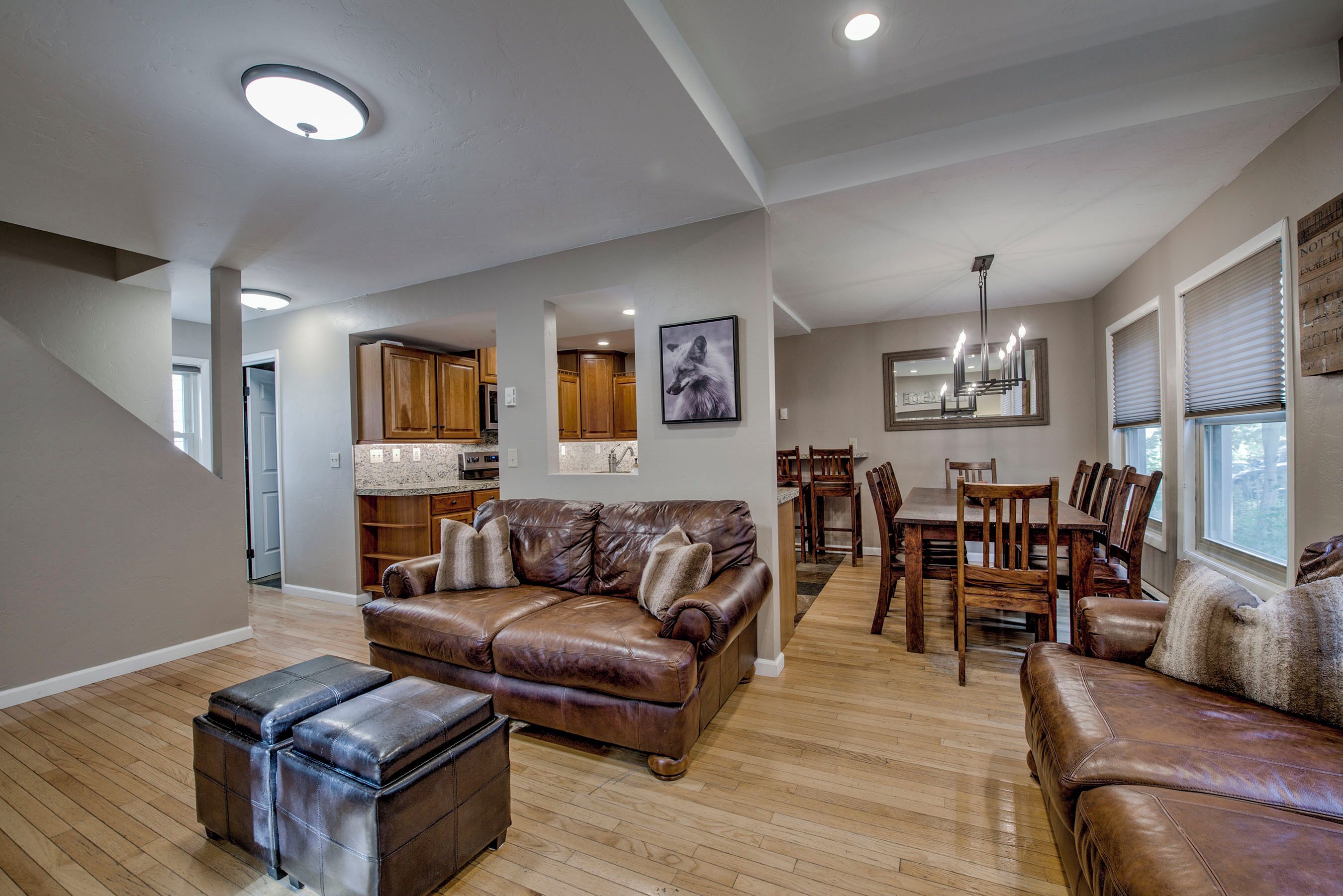 A spacious living room with a brown leather sofa, a dining area with wooden chairs, and a kitchen in the background.