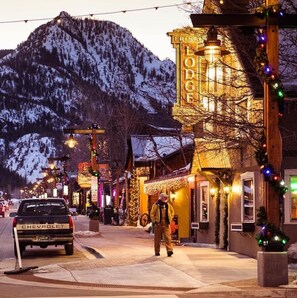 A street lined with buildings decorated with lights and garlands, a Chevrolet truck parked on the side, and a person walking.