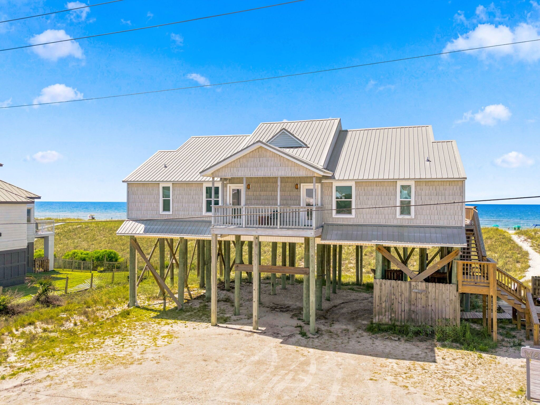 A beachfront house with a balcony, wooden deck, and a sandy driveway.