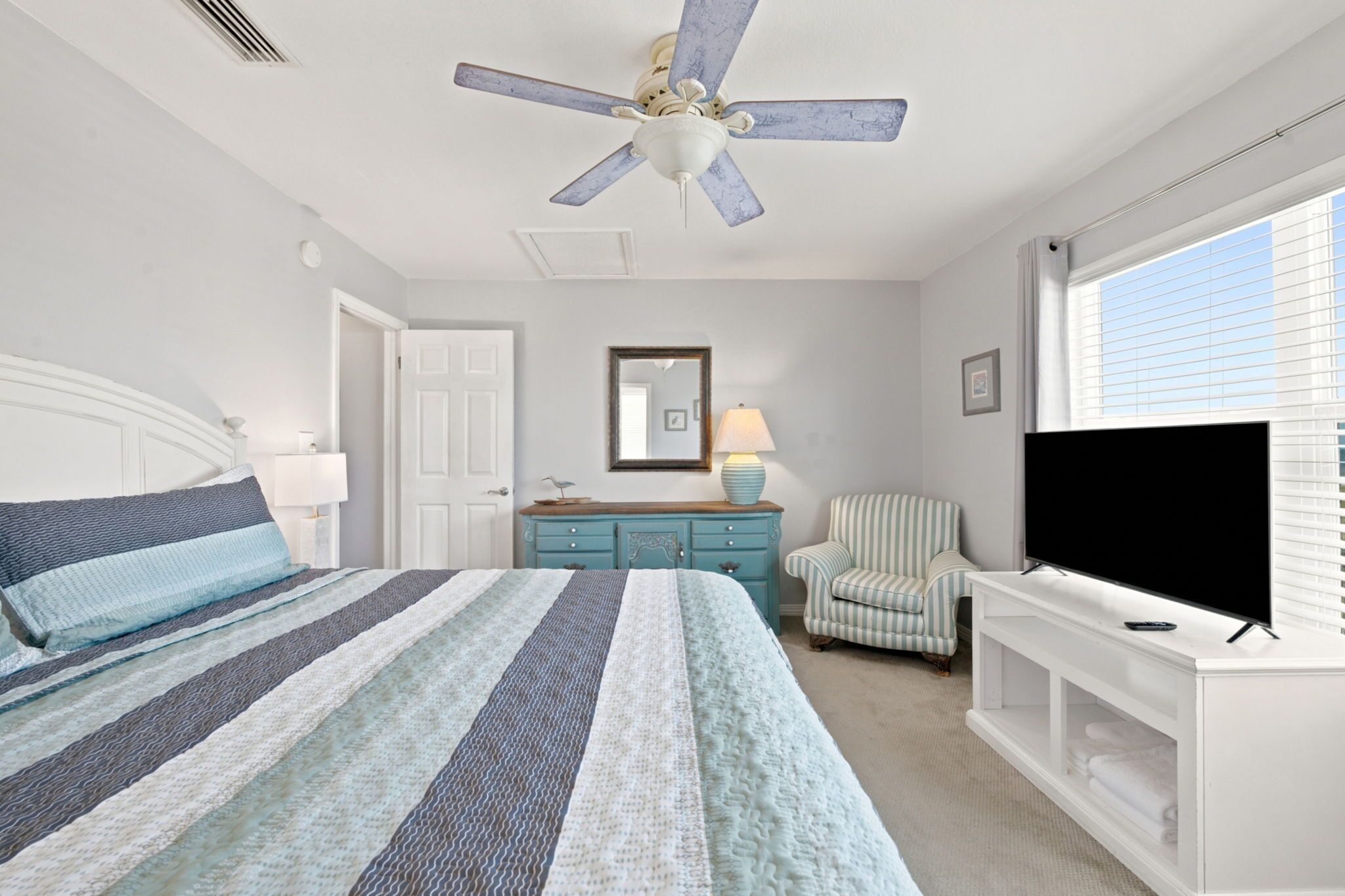 A bedroom with a bed, a dresser, a chair, a television, and a ceiling fan.