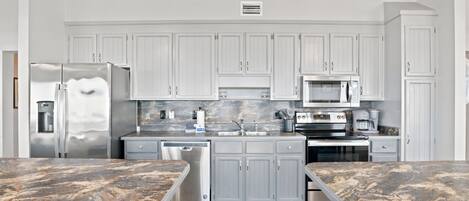 Cocina moderna con armarios blancos, electrodomésticos de acero inoxidable y encimera de mármol.