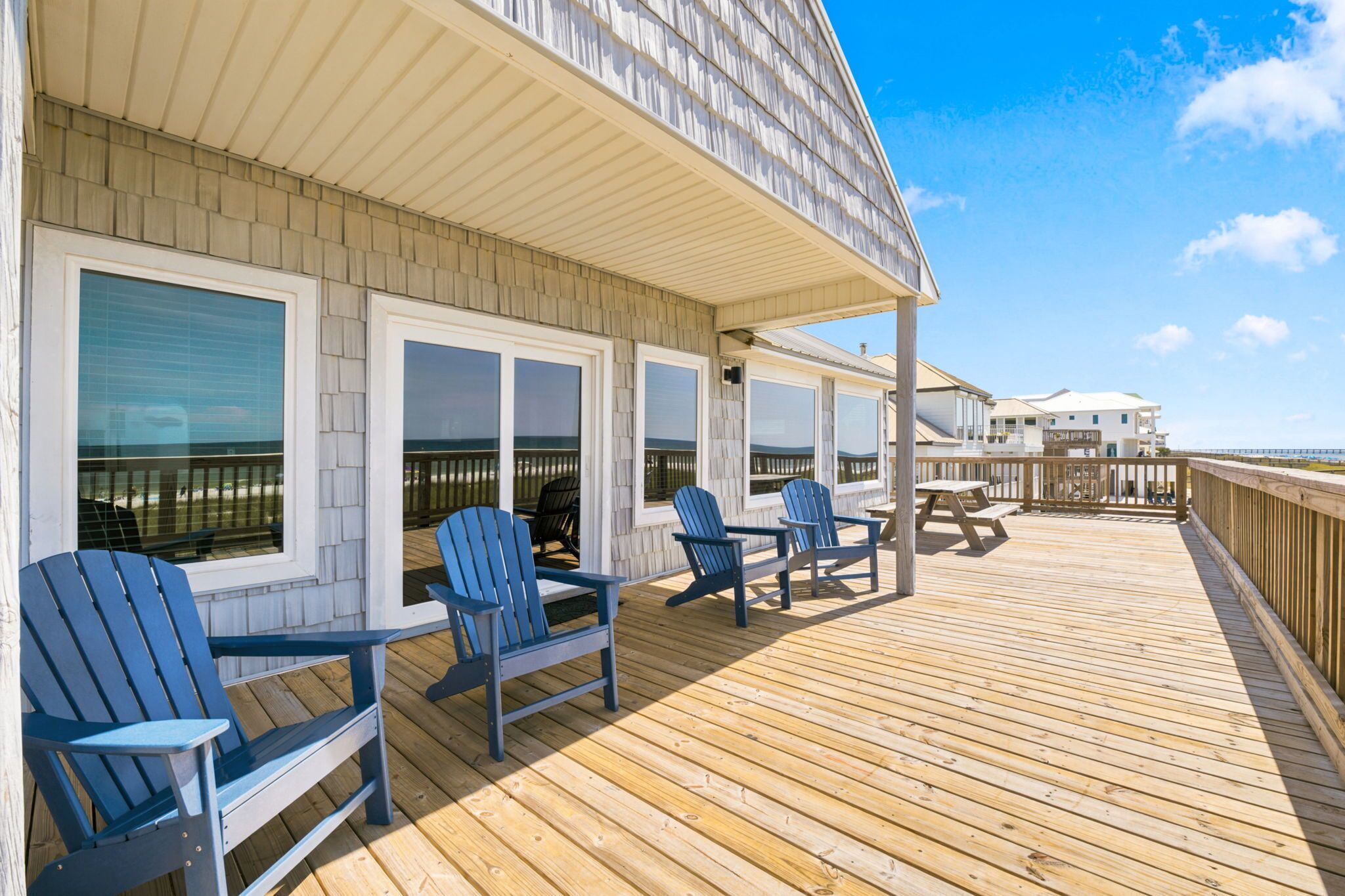 A wooden deck with chairs and a table, overlooking a beach.