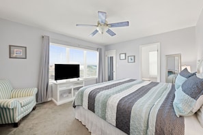 Une chambre à coucher avec un lit, une chaise, un téléviseur et un ventilateur de plafond.