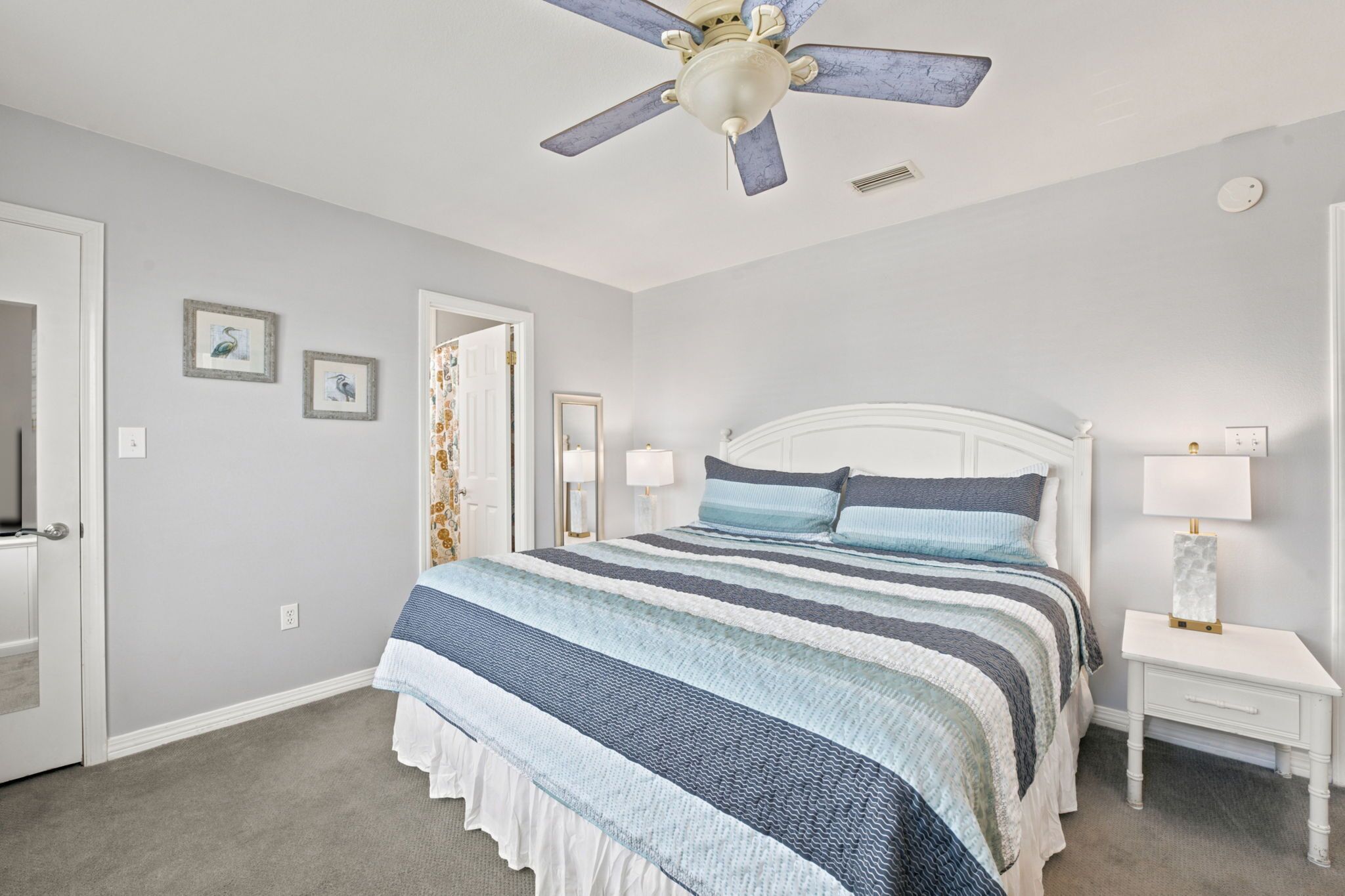 A bedroom with a bed, a ceiling fan, a nightstand, and a door.