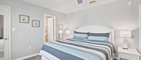 A bedroom with a bed, a ceiling fan, a nightstand, and a door.