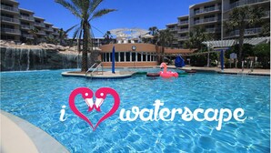 A swimming pool with a water slide, palm trees, and a building with balconies in the background.