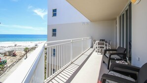 A balcony with a view of the beach, white railing, and two chairs.