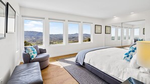 A bedroom with a large bed, a gray armchair, a bench, and multiple windows offering a view of the countryside. - As featured on CBS's Staycation!
Luxury Retreat Overlooking Sonoma Valley (Glen Ellen)