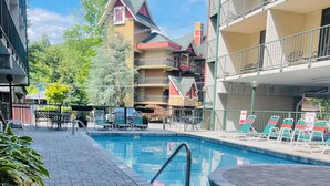 Una piscina con un sendero de ladrillos que la lleva a ella, rodeada de sillas de descanso y un edificio con balcones.